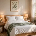 White bedding with sage green throw, light oak bed, bedside lamps and botanical print